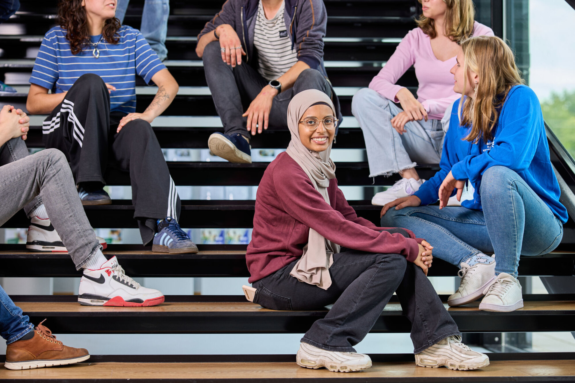 studenten zitten op trap in schoolgebouw en kijken naar de camera